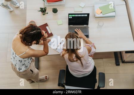 Top view of two businesswomen working together at the office, analyzing data using lap top. Stock Photo
