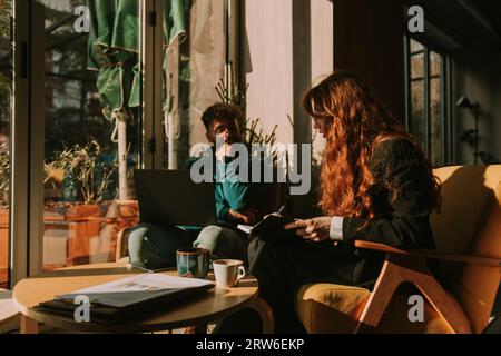 Young business people creating new sales plan while working remotely at the coffee bar. Woman with long red hair writing in notebook Stock Photo