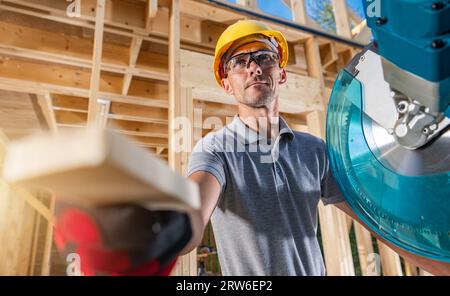 Wooden Construction Contractor Worker and His Job. Operating Professional Circular Saw Stock Photo