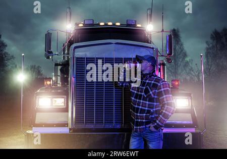 https://l450v.alamy.com/450v/2rw6ewt/professional-truck-driver-drinking-coffee-in-front-of-his-semi-truck-tractor-during-evening-stop-break-2rw6ewt.jpg