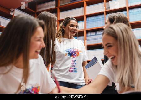 A diverse group of university students studying in a library. They collaborate, discuss subjects, and work on projects together, supported by professo Stock Photo