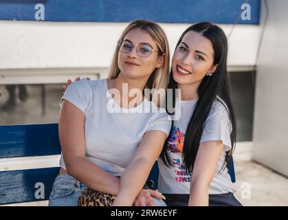 A portrait shot of two lovely female students taking a break from classes sitting on bench outdoors. Stock Photo