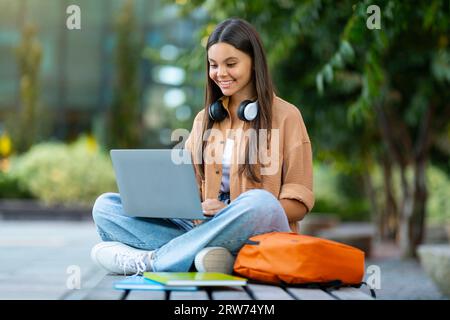 Cheerful young woman student doing homework at park Stock Photo