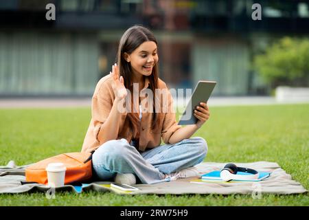 Cheerful young woman student chilling at park, using digital tablet Stock Photo