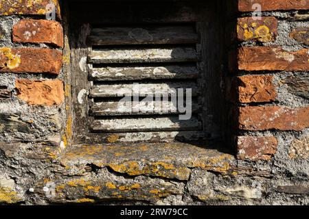 Weathered stone wall with lichen-covered sill and wooden louvre vent in historic Cornish building Stock Photo