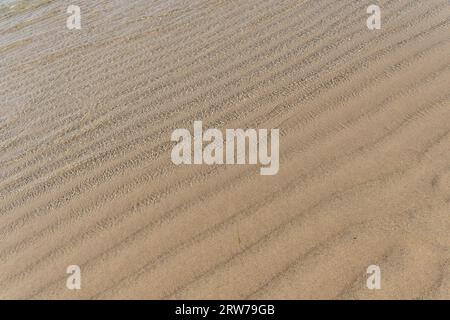 Rippled sand patterns on Cornish beach with gentle waves at water's edge Stock Photo