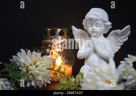 Angel, votive candle and flowers on black background Stock Photo