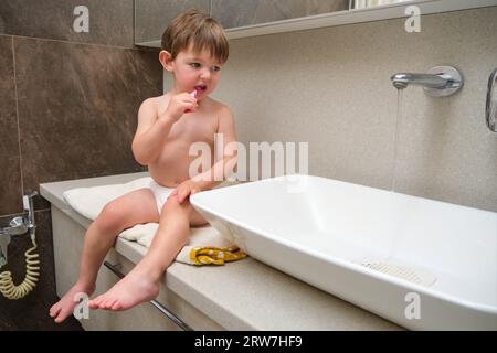 In the bathroom, the baby boy is learning to brush his teeth using a toothbrush. Kid aged two years (two-year-old boy) Stock Photo