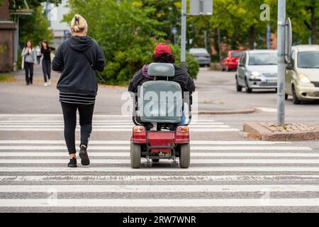 person in a electric wheelchair crossing a road Stock Photo