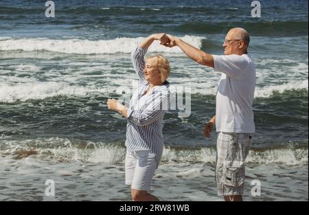 Happy elderly couple dancing on the seashore. In the background, the shore and sea waves. Stock Photo