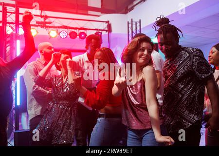 Passionate man and woman couple dancing together and moving to music beats in nightclub. African american boyfriend and caucasian girlfriend partying on dancefloor at discotheque Stock Photo
