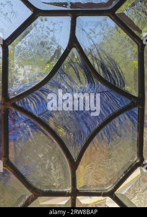 Photo taken through leaded glass panels shows green scenery with decorative metal framework. Glass is beveled in abstract shapes with light reflection. Stock Photo
