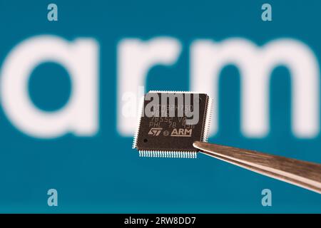 ARM company logo seen on STM32 microchip hold in tweezers and blurred ARM company logo on the background. London, United Kingdom, September 17, 2023 Stock Photo