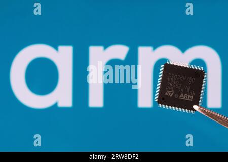 ARM logo seen on STM32 microchip hold in tweezers and blurred ARM company logo on the background. London, United Kingdom, September 17, 2023 Stock Photo