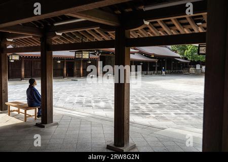 A Japanese man in traditional clothing sits contemplating  the main shrine building at the inner courtyard of the Meiji Jingu located inside a 170 acres forest park, in Shibuya, Tokyo, Japan. The Shinto shrine is dedicated to the spirits of Emperor Meiji and his wife, Empress Shoken. Stock Photo