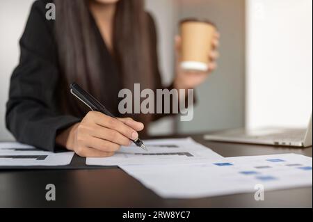 Close-up image of a professional businesswoman working on a business financial report at her desk, holding a pen, pointing a pen at the report paper. Stock Photo