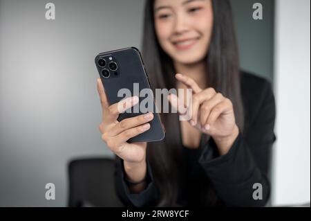 Close-up image of a happy and satisfied Asian businesswoman checking messages or reading an unexpected email on her smartphone while sitting in the of Stock Photo
