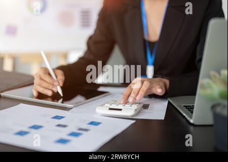 Close-up image of a professional female accountant or financial assistant working at her desk, analyzing financial data on reports, using a calculator Stock Photo