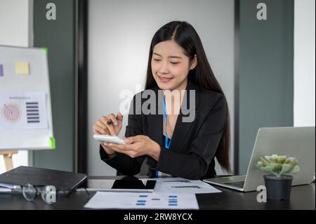 A beautiful and professional Asian businesswoman or female accountant using a calculator, analyzing business financial data on reports, working at her Stock Photo