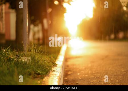 It's raining in the city. Sun-lit city street, road and raindrops at sunset. Stock Photo