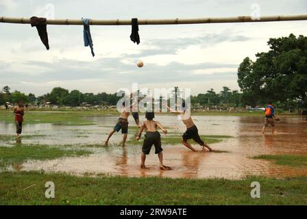 Children play football on a field, which is partly flooded and is located between two public cemetery sites in Pondok Kelapa, East Jakarta, Jakarta, Indonesia. Stock Photo