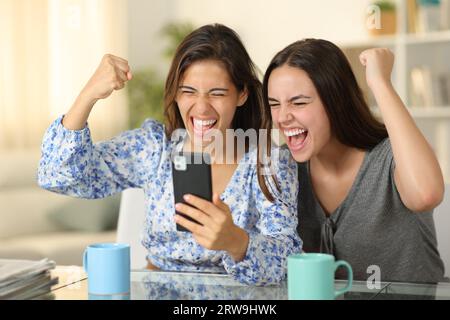 Excited women checking phone celebrating success at home Stock Photo