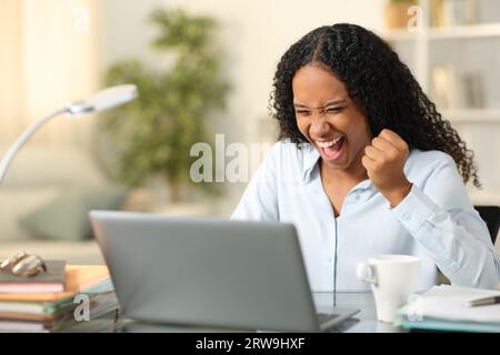 Excited black teleworker checking online news on laptop at home Stock Photo