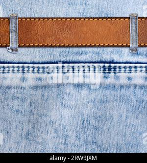 Blue denim background with leather belt. Horizontal or vertical backdrop with light blue color denim jeans fabric texture and brown leather strap. Moc Stock Photo