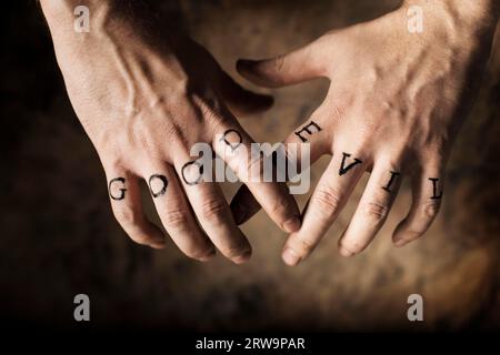 Man with Good and Evil (fake) tattoos on his hands Stock Photo