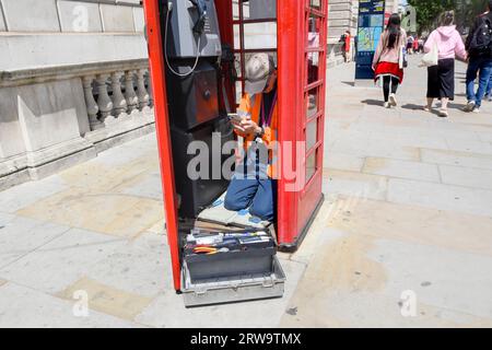 London, UK. Repair man on his mobile phone as he repairs a phone box in Parliament Square Stock Photo