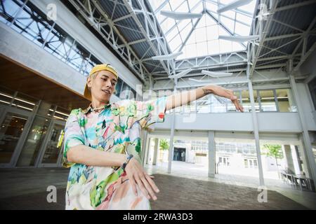 Action portrait of smiling young Asian man dancing in urban city building, copy space Stock Photo