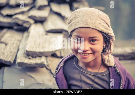 Dolpo, Nepal, circa May 2012: Young girl with beautiful big brown eyes wears headcloth and violet sweatshirt in Dolpo, Nepal. Documentary editorial Stock Photo