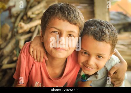 Damak, Nepal, circa May 2012: Two young brothers with brown eyes hug and smile to photocamera at Nepali refugee camp in Damak, Nepal. Documentary Stock Photo