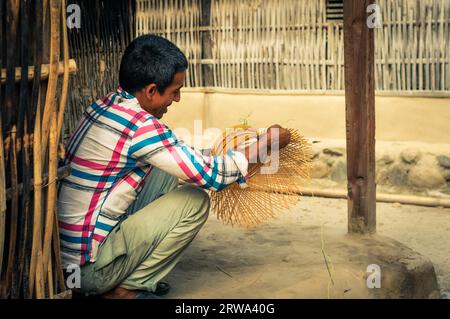 Damak, Nepal, circa May 2012: Native man in checked shirt kneels and weaves hat at Nepali refugee camp in Damak, Nepal. Documentary editorial Stock Photo