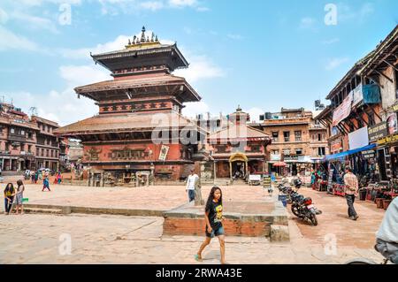 Bhaktapur, Nepal, circa June 2012: People walk through marketplace with high old building in centre of square in Bhaktapur, Nepal. Documentary Stock Photo