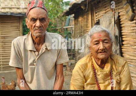 Damak, Nepal, circa May 2012: Old man with wrinkled face with cap on his head frowns and poses with his wife to photocamera at Nepali refugee camp in Stock Photo