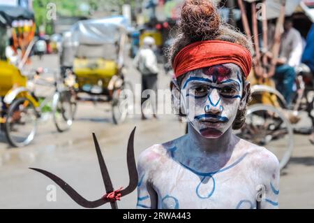 Silchar, Assam, circa April 2012: Young boy with orange headband and with body covered in white powder and colours holds pitchfork in Silchar, Assam. Stock Photo