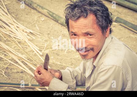 Damak, Nepal, circa May 2012: Old man dressed in white clothes holds knife at Nepali refugee camp in Damak, Nepal. Documentary editorial Stock Photo