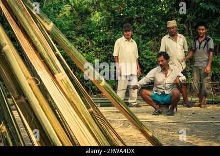 Damak, Nepal, circa May 2012: Three native men stand behind sitting man with knife and they look to photocamera at Nepali refugee camp in Damak Stock Photo