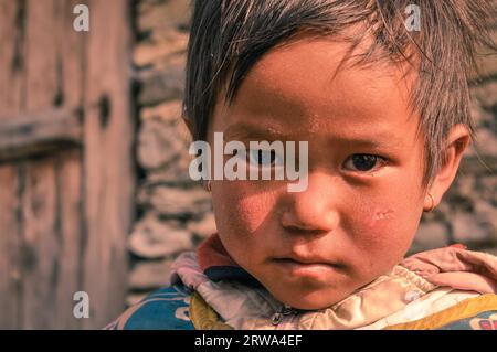 Beni, Nepal, circa May 2012: Small girl with short brown hair and brown eyes wears earrings and looks sadly to photocamera in Beni, Nepal. Stock Photo