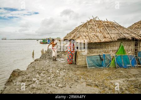 Sunderban, Bangladesh, circa July 2012: Woman and man stand in mud near river in front of their simple house in Sunderban, Bangladesh. Documentary Stock Photo