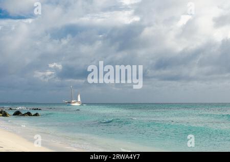 Picture showing a big sailboat on sea navigating towards the beach. The image was taken from Arashi Beach, Aruba, in the Caribbean Sea Stock Photo