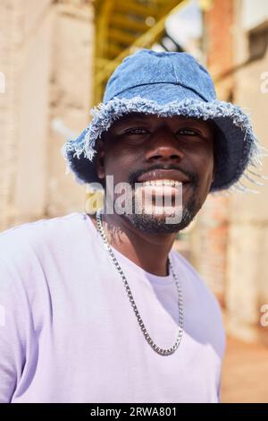 Vertical portrait of young Black man smiling at camera in urban setting lit by sunlight Stock Photo