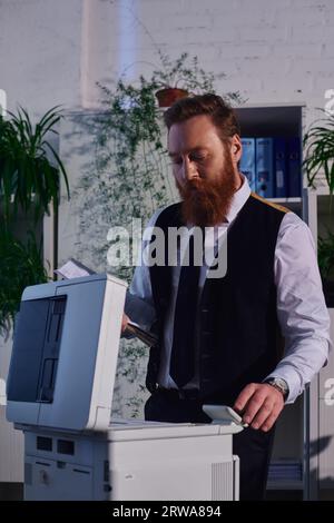 focused bearded businessman copying documents on copier machine while working late in office Stock Photo