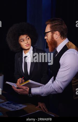interracial entrepreneurs looking at each other while working with documents at night in office Stock Photo