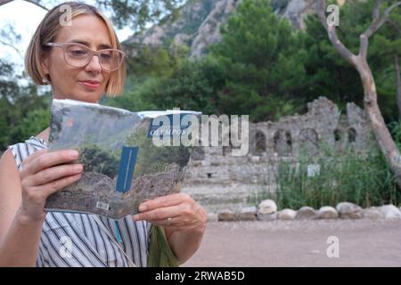 A female tourist reading a Turkish guidebook on Olympos while in front of a building that is on the cover. Stock Photo