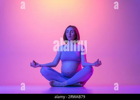 Sporty pregnant woman doing yoga against color background Stock Photo