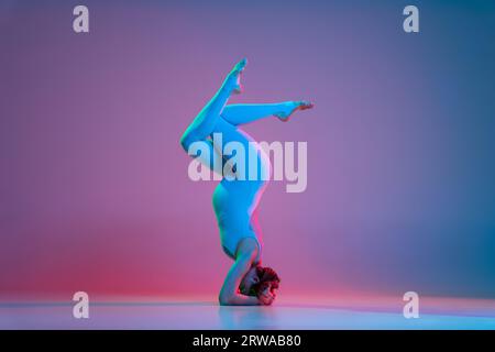 Sporty pregnant woman doing headstand against color background Stock Photo