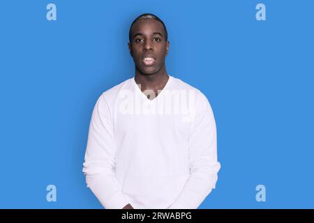 Portrait of cheerful young african-american guy wearing white casual sweater posing isolated on blue background. Carefree young millennial man looking Stock Photo