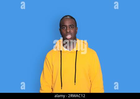 Young sad frustrated worried man in yellow hoodie looking camera isolated on blue wall background studio portrait. People sincere emotions lifestyle c Stock Photo